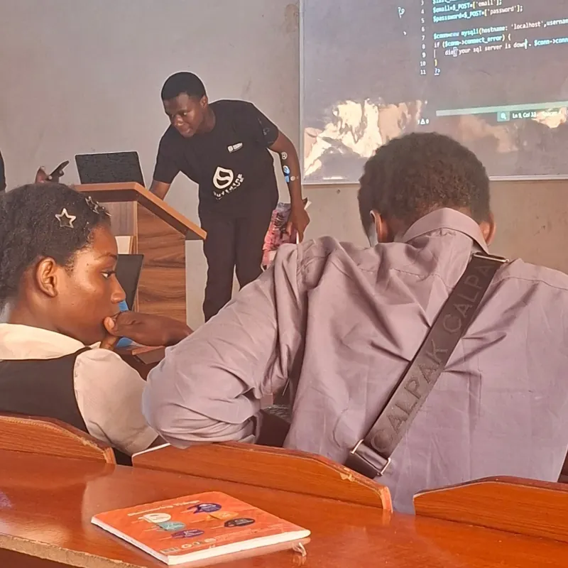 Ezechukwu at the front of a classroom teaching, with code projected on the screen behind him